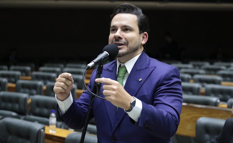 Deputado Capitão Alberto Neto fala ao microfone. Ele é claro, tem o cabelo escuro, barba e bigode, e usa um terno azul-marinho