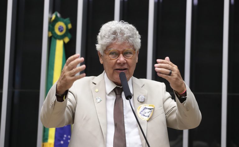 Deputado Chico Alencar fala ao microfone. Ele é claro, tem o cabelo cacheado e grisalho, e usa um terno bege