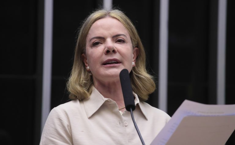 Uma mulher loira usando uma blusa branca fala ao microfone