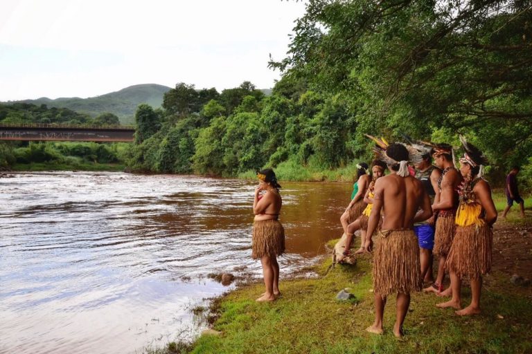 Índios observam um rio cheio de lama