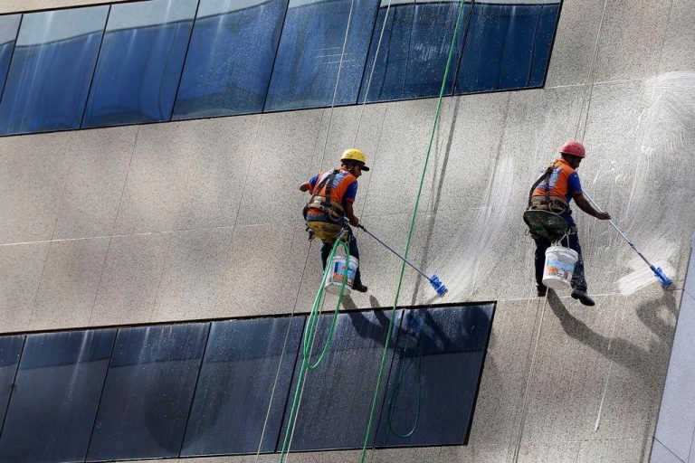 Trabalhadores presos por cordas limpando fachada de um prédio