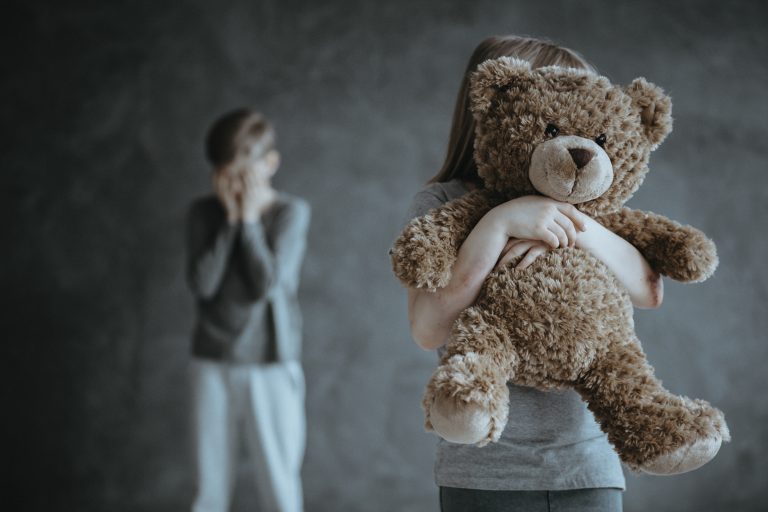 Menina se escondendo atrás de um urso de pelúcia e menino escondendo o rosto com as mãos