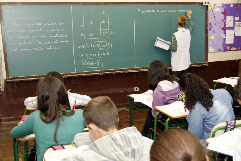 Alunos copiam o dever que a professora escreve no quadro negro