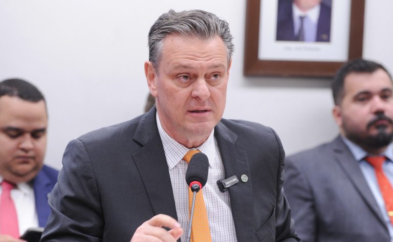 O ministro da Agricultura fala ao microfone. Ele é branco, tem o cabelo grisalho, usa um terno escuro, camisa clara e gravata laranja