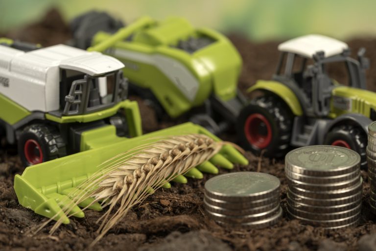 Máquinas agrícolas em miniatura, um ramo de trigo e moedas em cima da terra