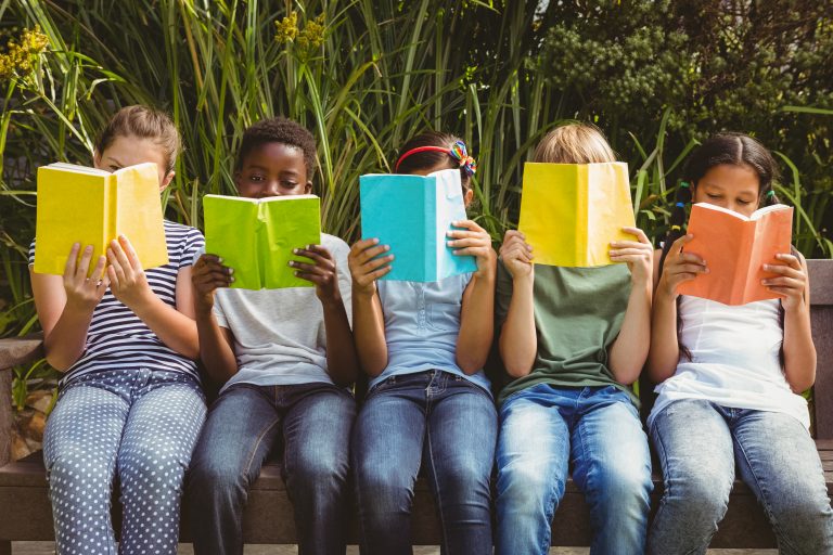 Crianças sentadas lendo livros de capas coloridas