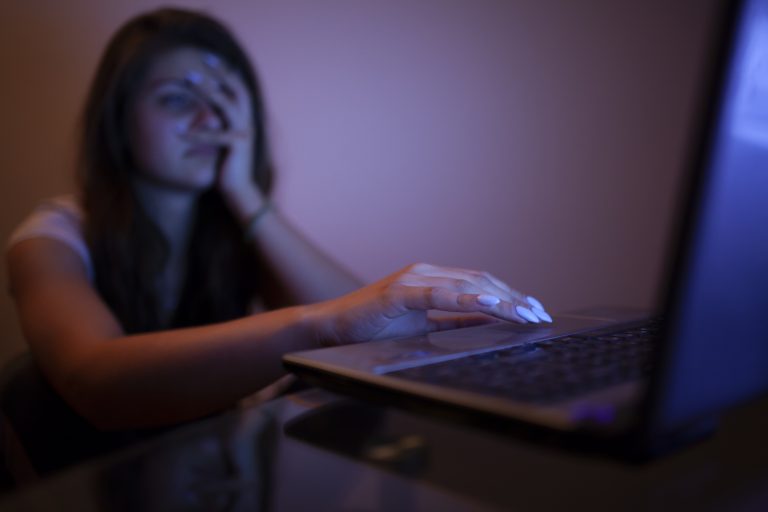 Uma mulher está com uma mão no rosto e a outra mão no teclado de um laptop