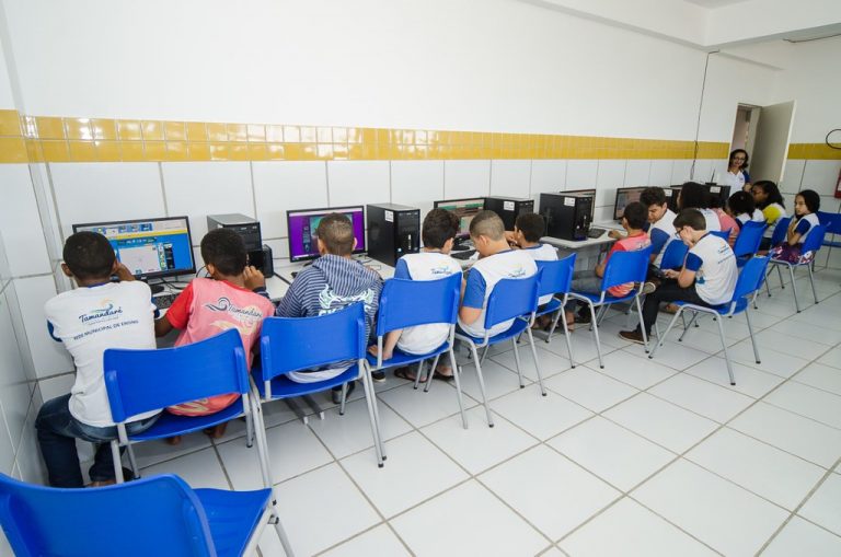 Alunos sentados em frente a computadores, em aula no laboratório de informática